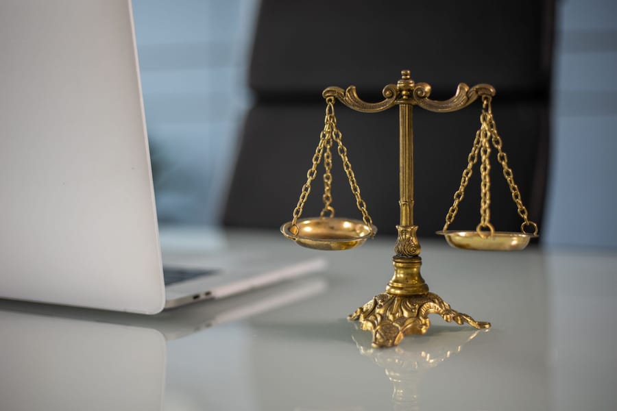 A brass balance scale on a pale desk beside an open laptop.